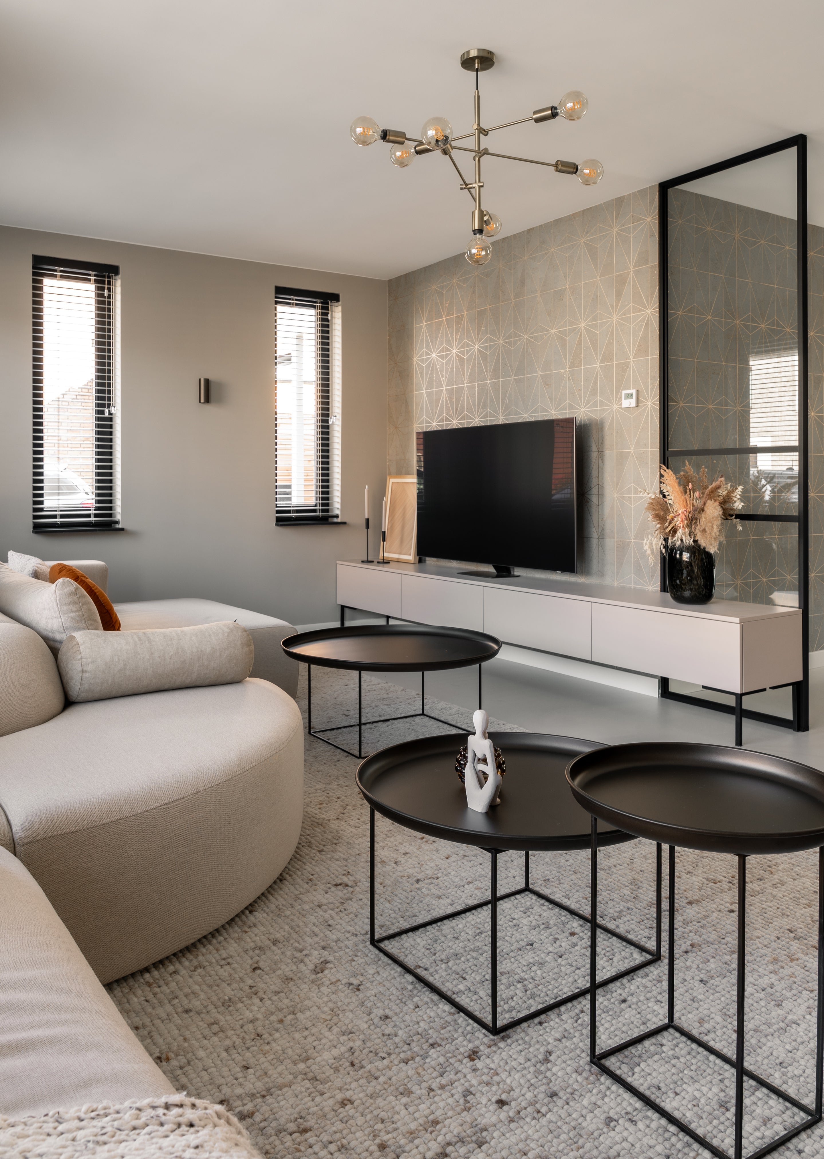 Moderne woonkamer met lichtgrijze vloer, ronde banken en zwarte salontafels, met tv-meubel en gouden hanglamp.