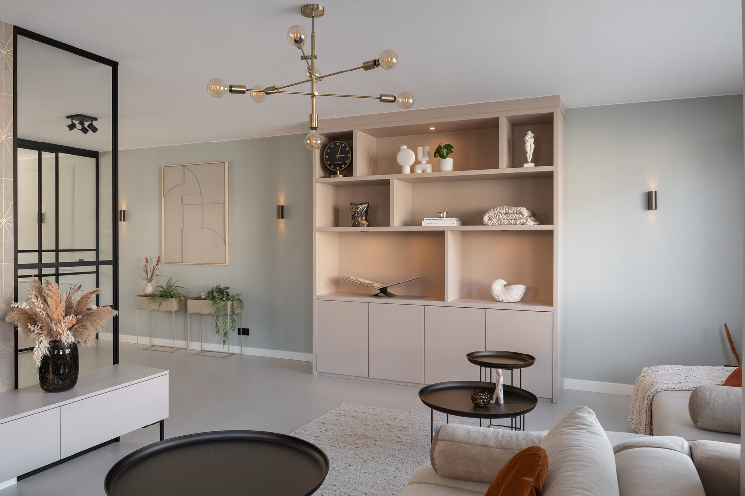 Lichte woonkamer met open kast vol decoratieve objecten, ronde tafels en moderne hanglamp.