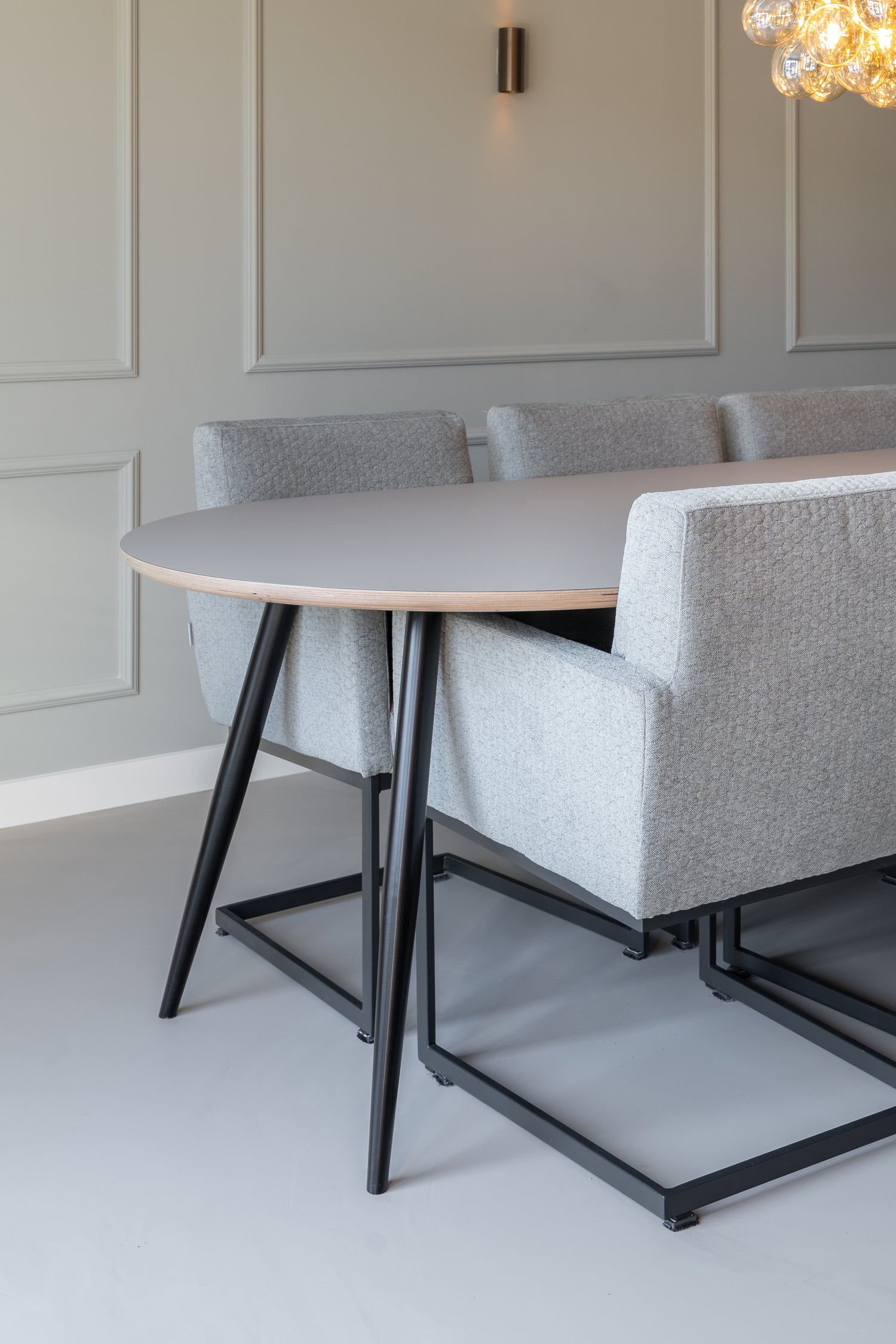 Moderne eethoek met ovale tafel en gestoffeerde stoelen op een strakke lichtgrijze gietvloer.