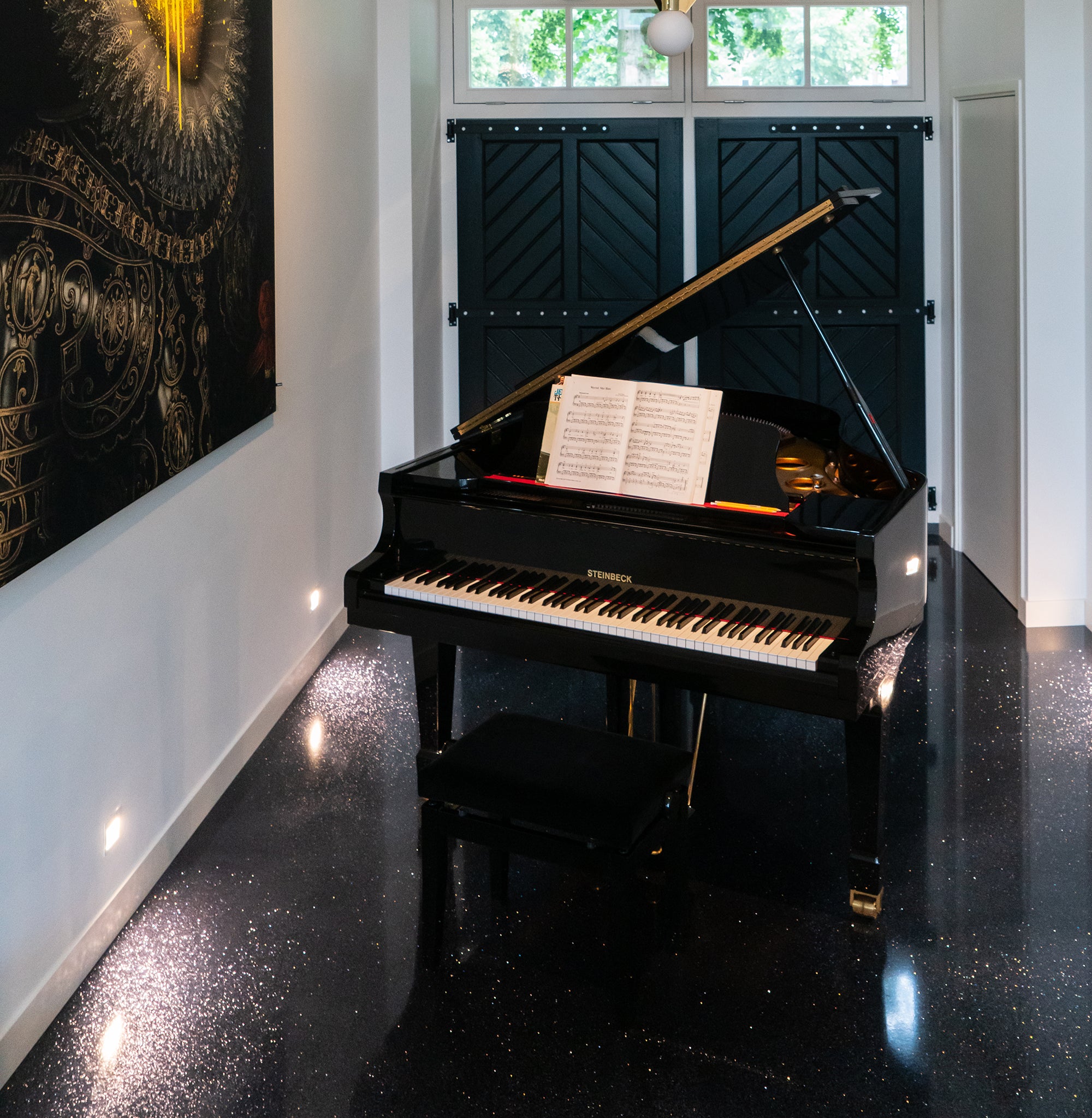 Zwarte vleugel met open bladmuziek op glinsterende zwarte vloer in een moderne ruimte met kunstwerk.