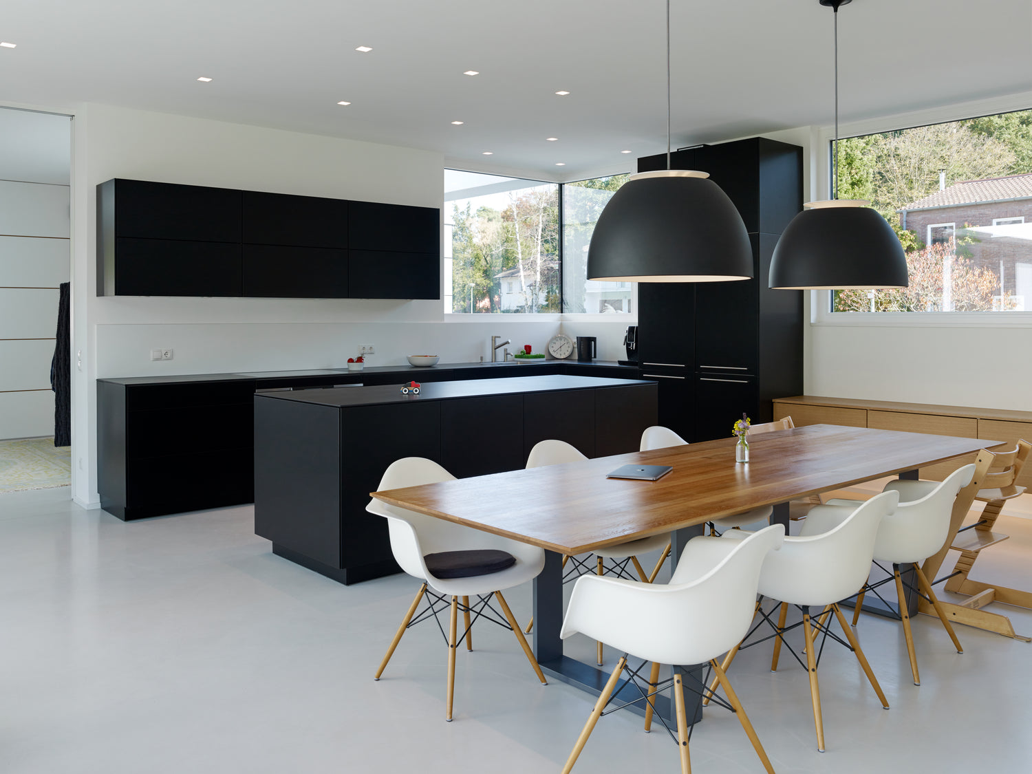 Lichtgrijze gietvloer in een keuken ruimte met zwarte keuken en zwart kookeiland, houten eettafel met witte stoelen.