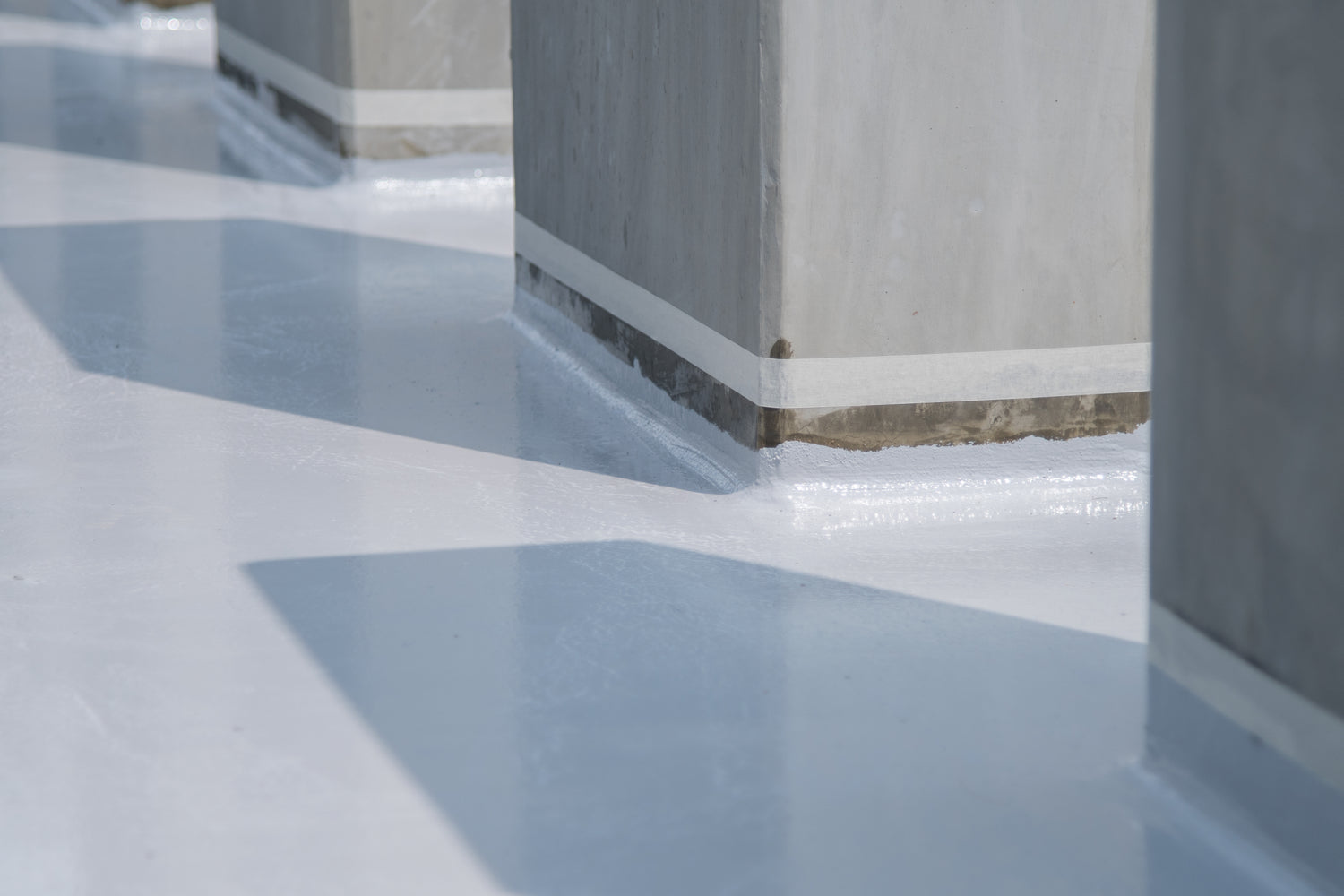 Detail van een strak afgewerkte vloer met betonnen kolommen en reflecterend oppervlak.