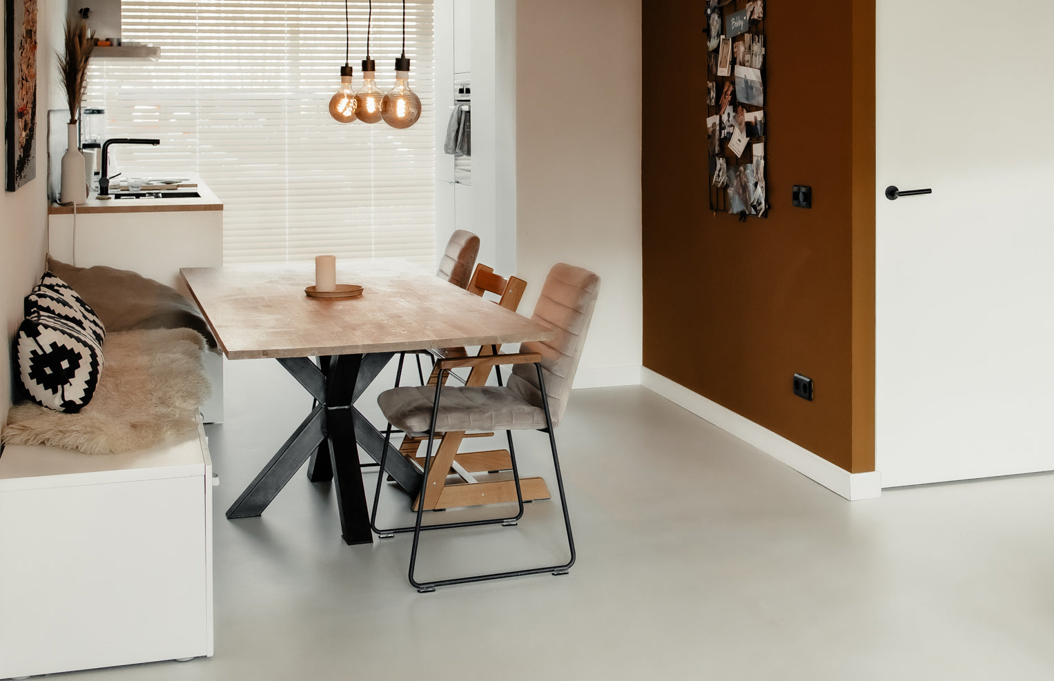Zijaanzicht van een lichte eethoek met een beige gietvloer, houten tafel en bruine accenten.