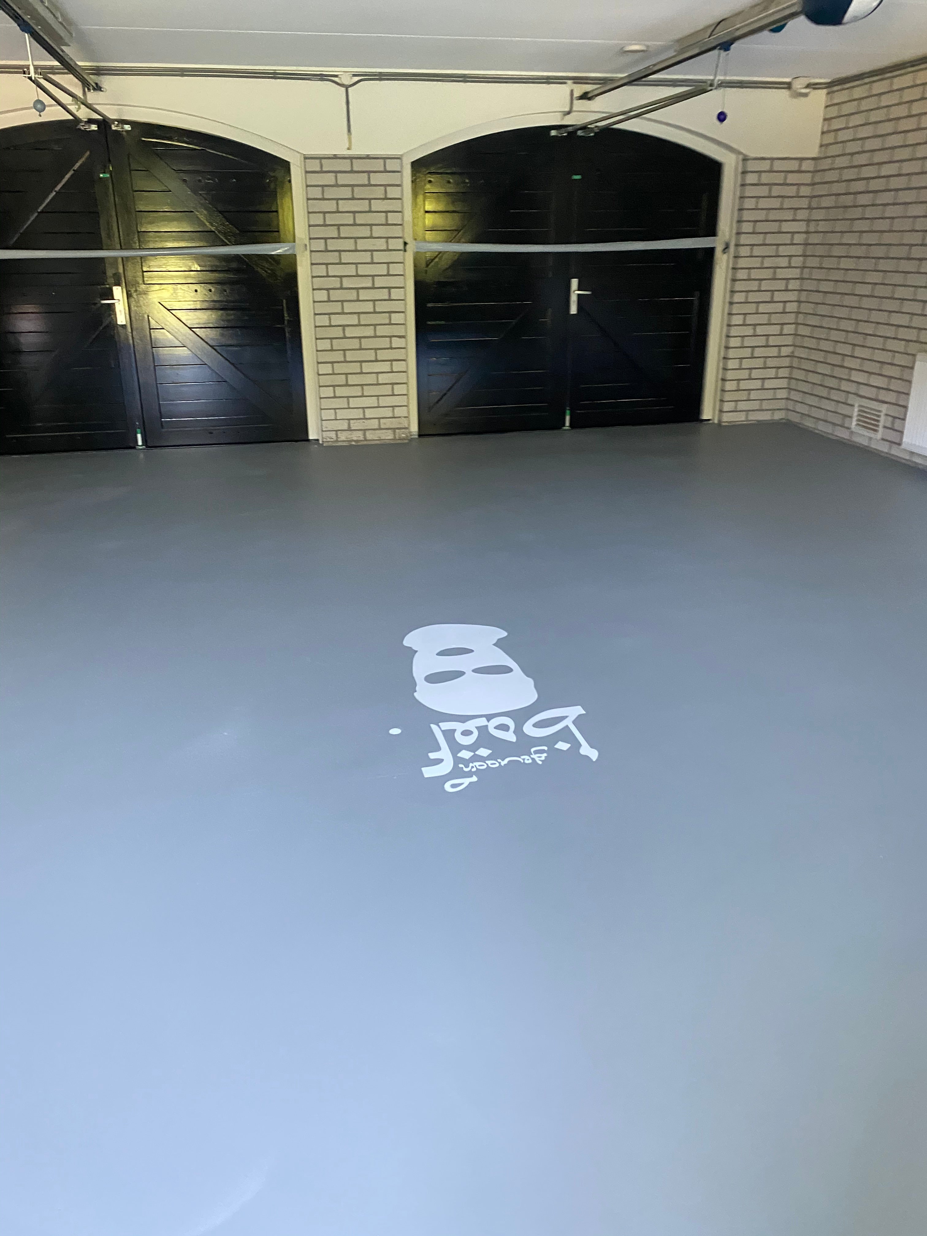 Ruime garage met grijze gietvloer en zwart-witte bakstenen muren, met kettlebell-logo op de vloer.