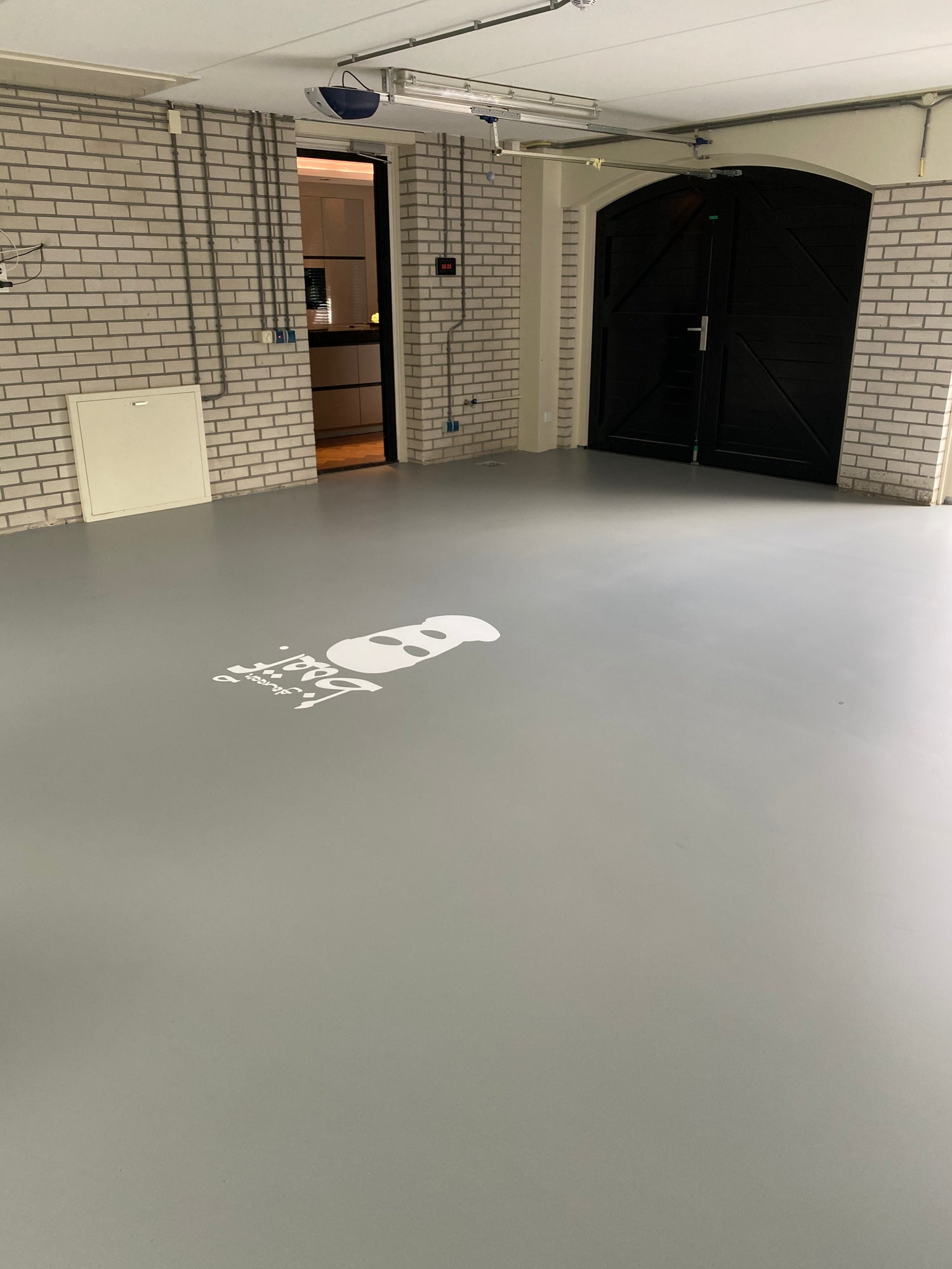 Lege ruimte met grijze gietvloer en witte bakstenen muren, met een zwart dubbele deur aan de achterkant.