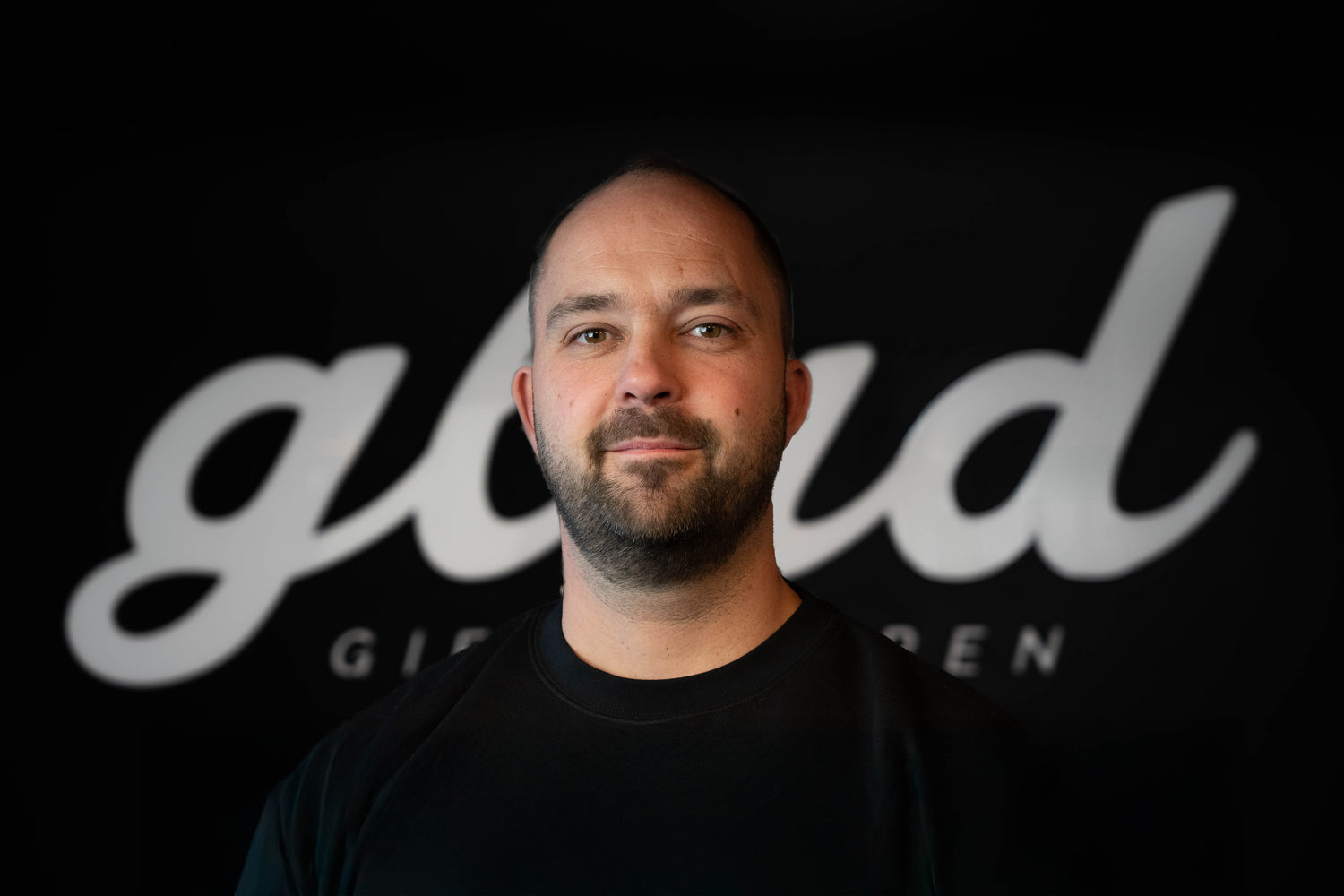 Eigenaar van Glad Gietvloeren op een zwarte achtergrond met het logo van Glad, de man kijkt vriendelijk