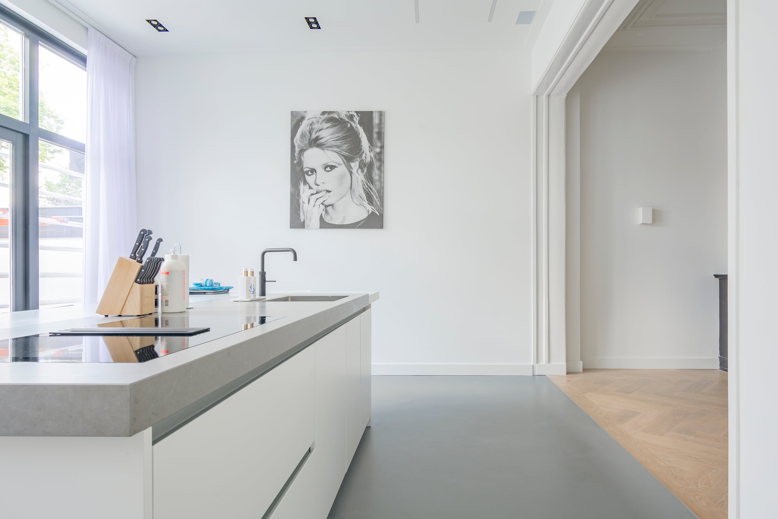 Lichte open keuken met een grijze gietvloer, modern wit kookeiland, verbonden met een visgraat houten vloer.