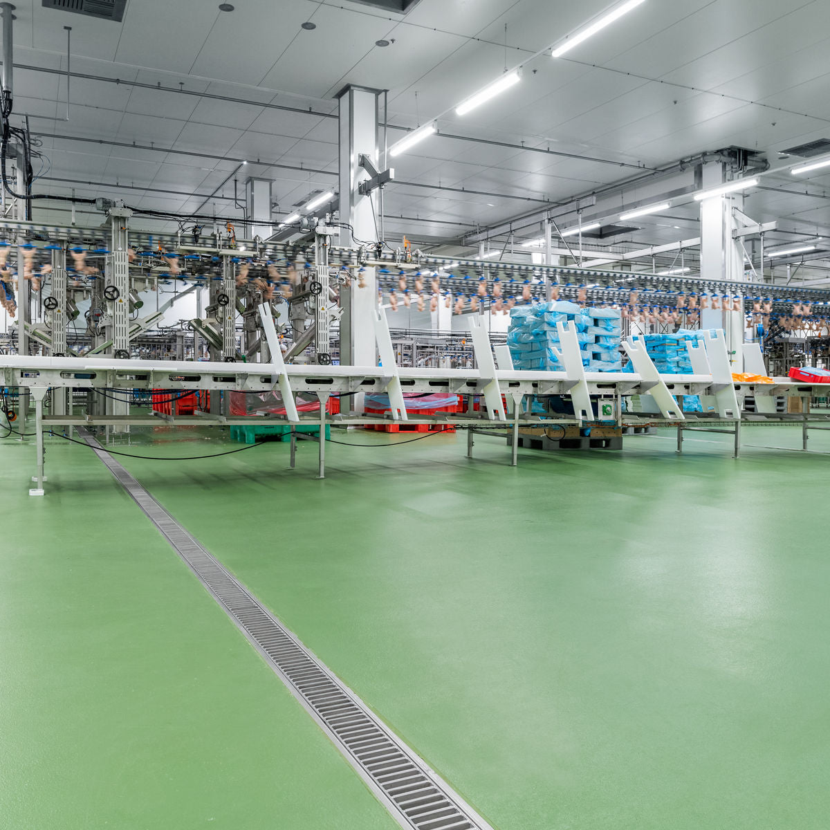 Industriële ruimte met groene Ucrete vloer, afvoergoot en lopende band voor voedselverwerking.