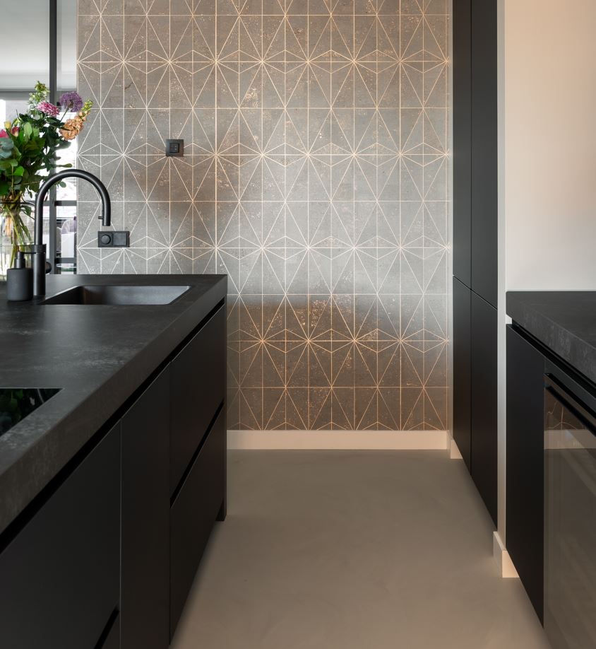 Strakke zwarte keuken met donker aanrechtblad en geometrische tegelwand als eyecatcher.