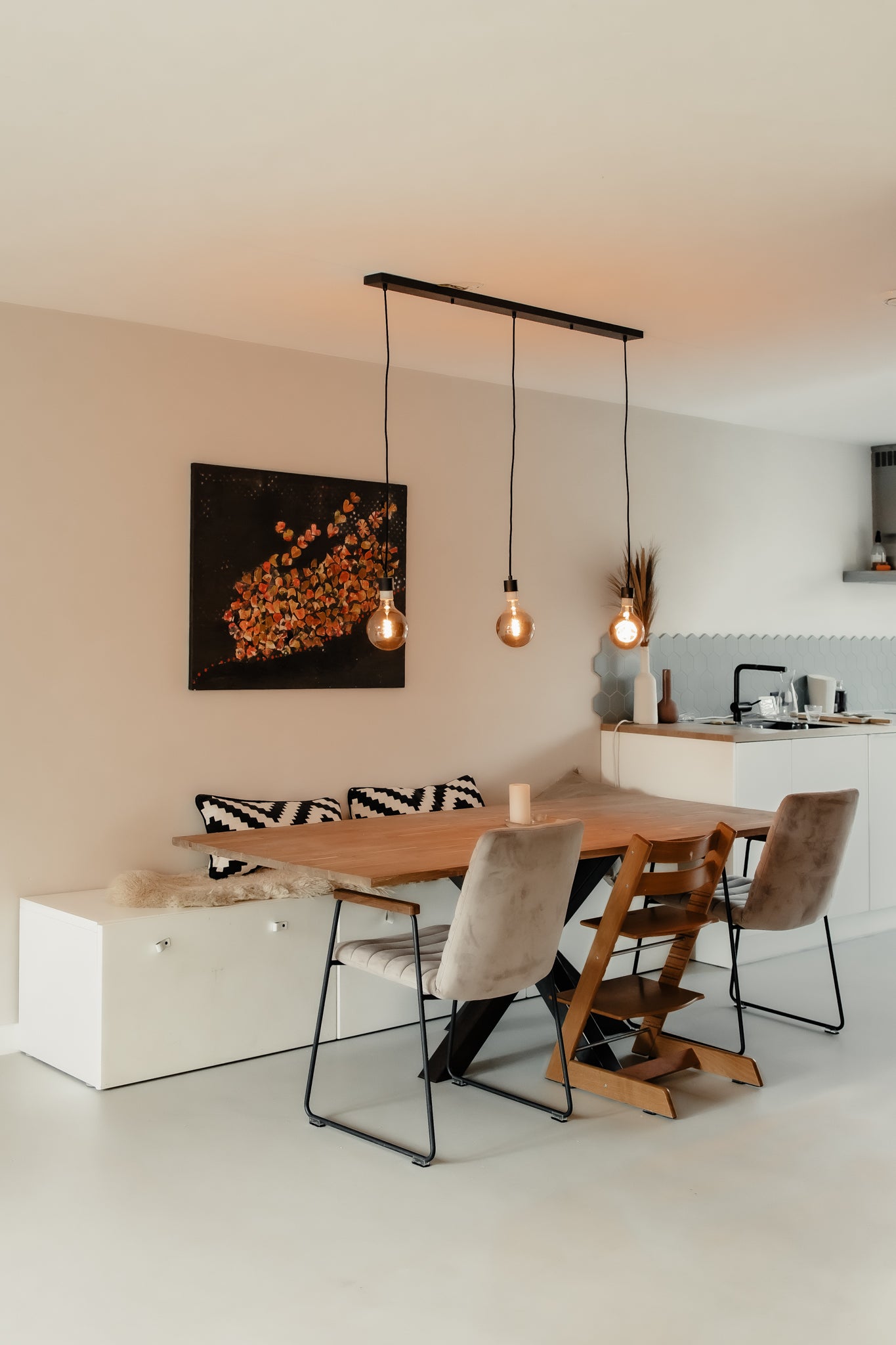 Gezellige eethoek met houten tafel, hanglampen en zitbank met kussens tegen een beige muur.