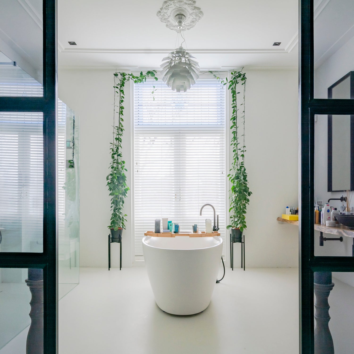 Vrijstaand bad voor groot raam met jaloezieën en hangplanten in stijlvolle, lichte naadloze badkamer van Glad Douche.