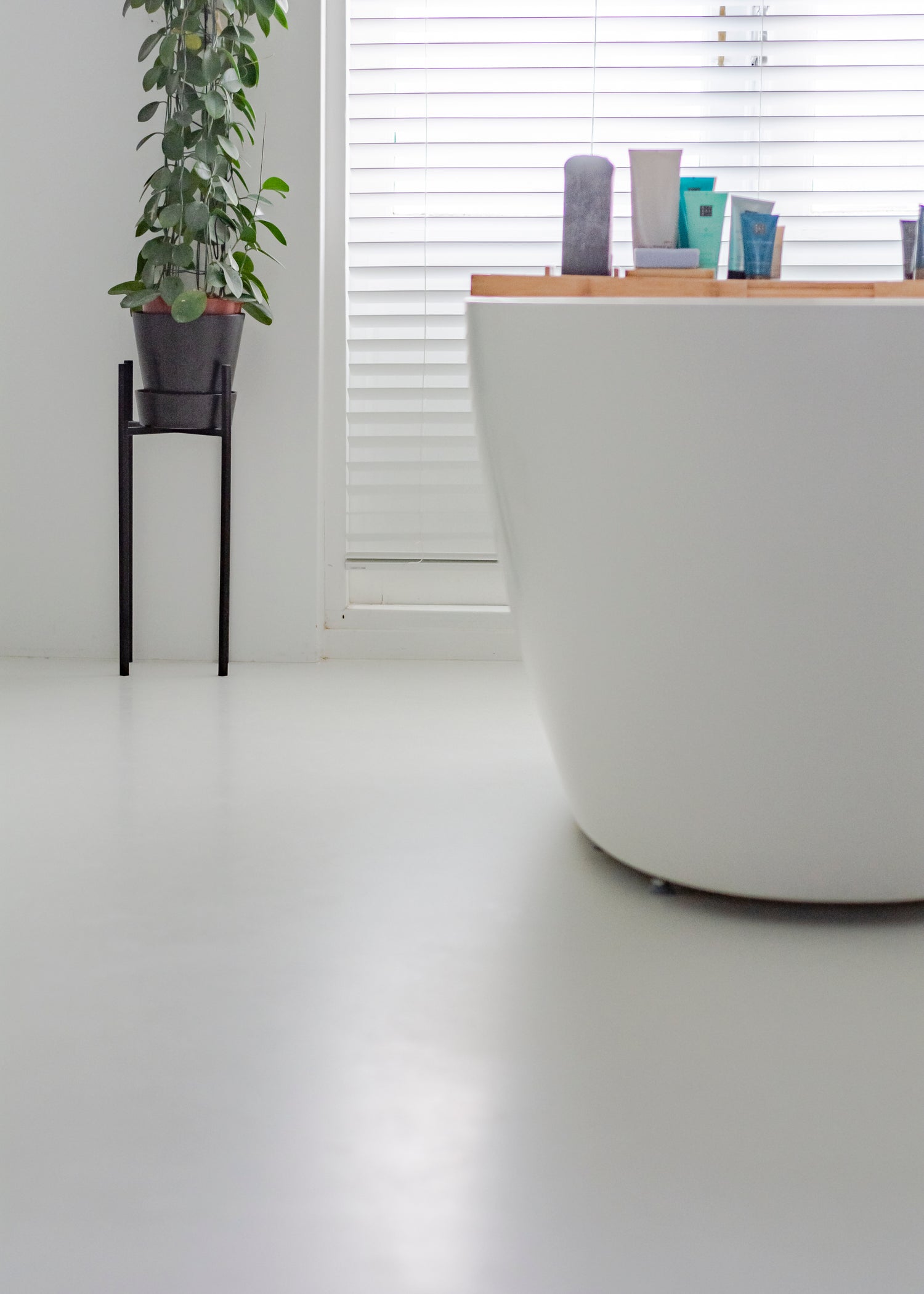 Minimalistische badkamer met wit bad, kamerplant en jaloezieën bij het raam.