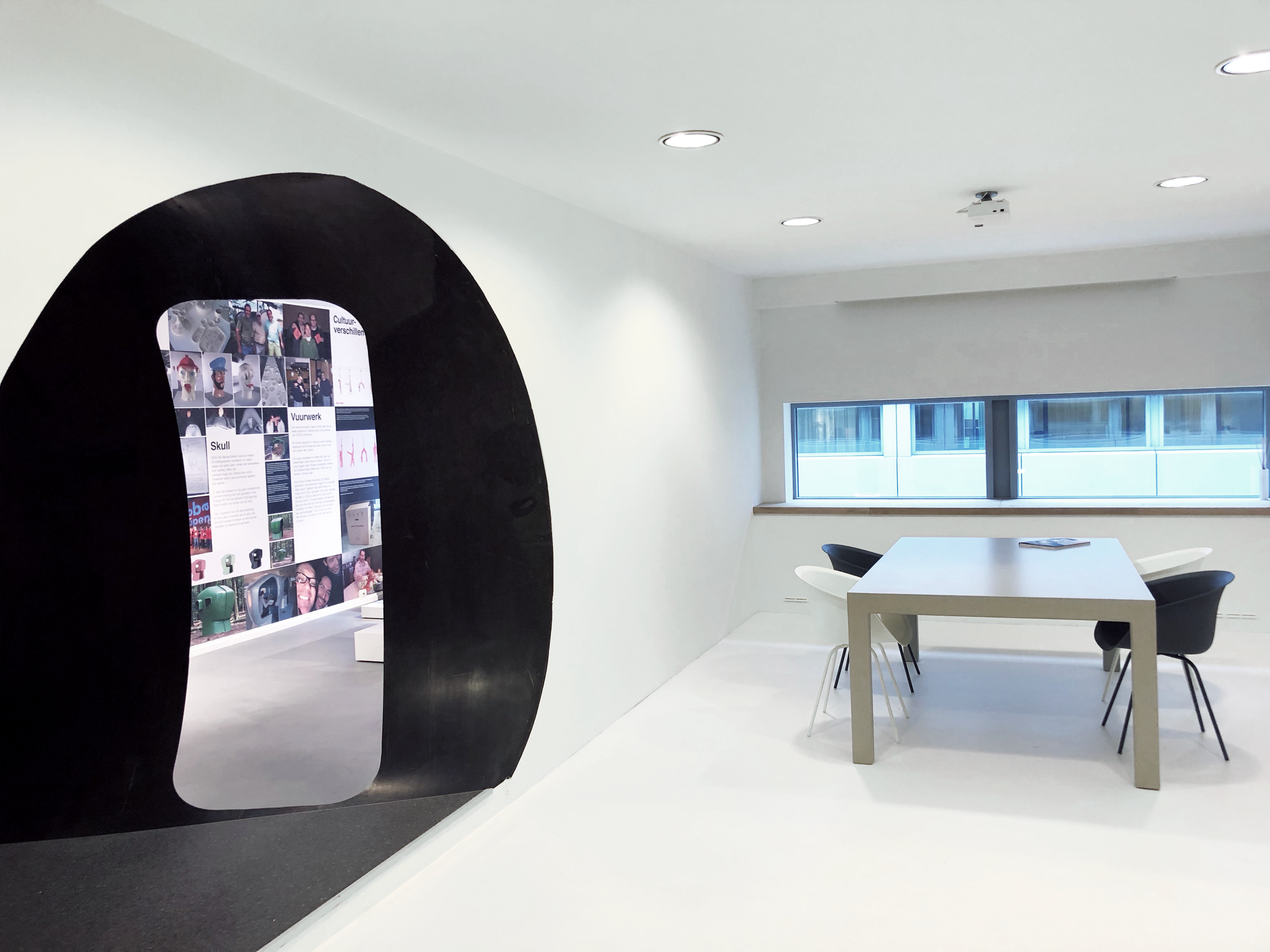 Moderne vergaderruimte met witte vloer en zwart kunstobject met opening in wand.