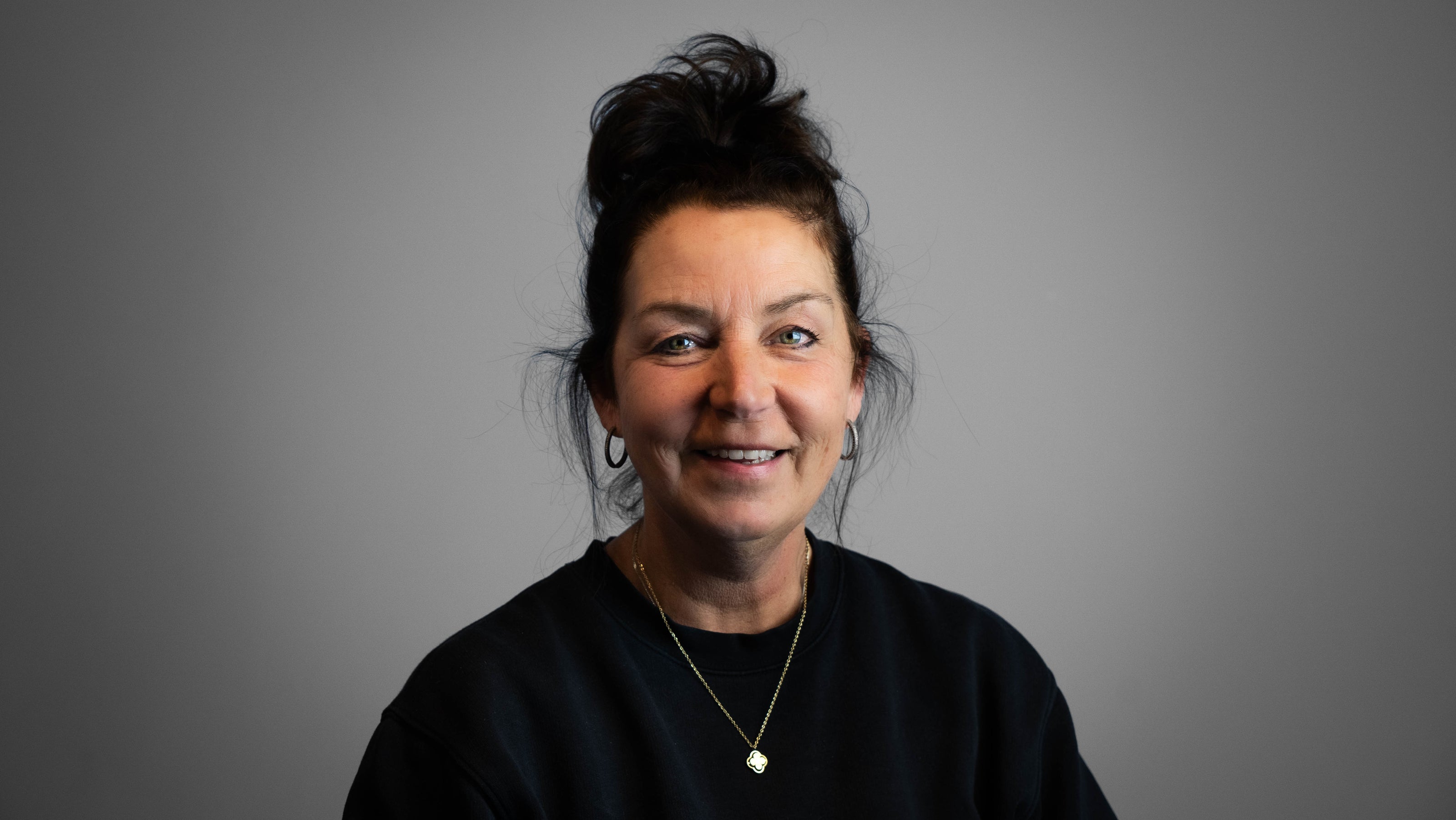 Vrouw met vriendelijke lach met zwart haar, zwarte trui op een grijze achtergrond. Medewerkster bij Glad Gietvloeren.