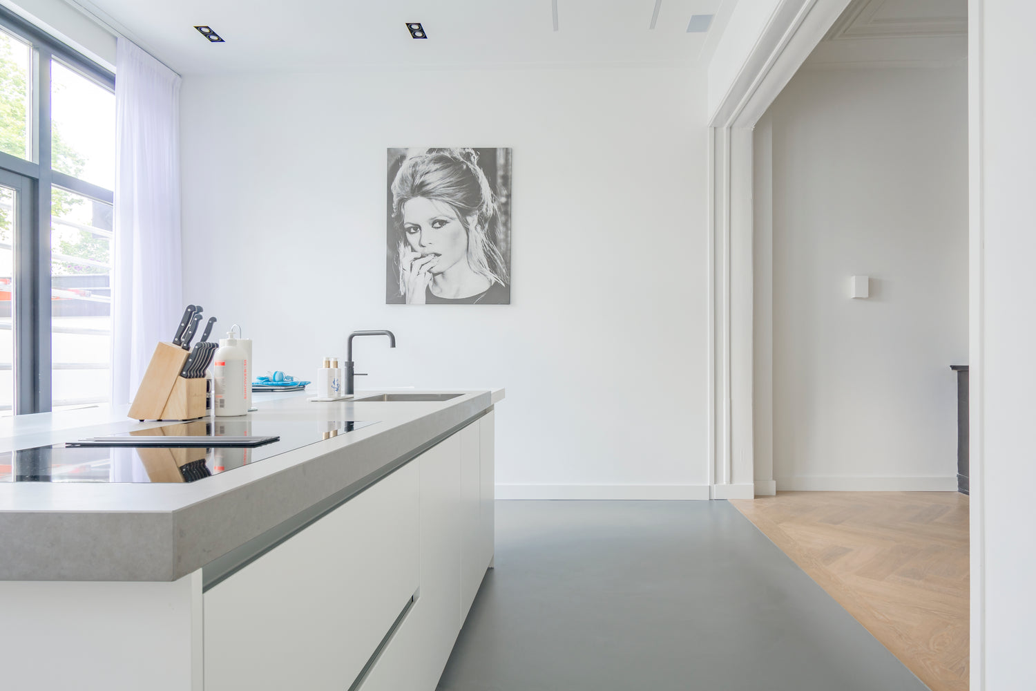 Lichte open keuken met een grijze gietvloer, modern wit kookeiland, verbonden met een visgraat houten vloer.