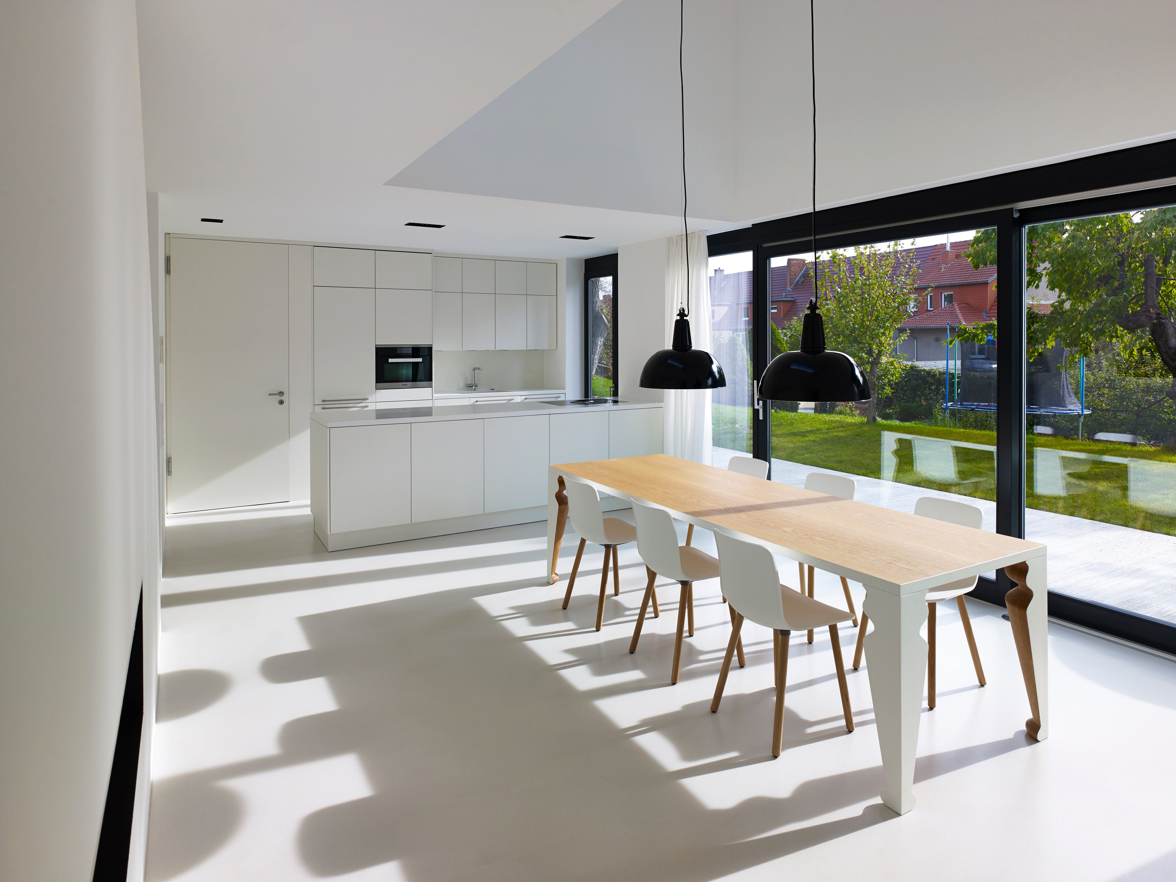 witte gietvloer in een keuken met eettafel en zwarte raamkozijnen en twee zwarte hanglampen