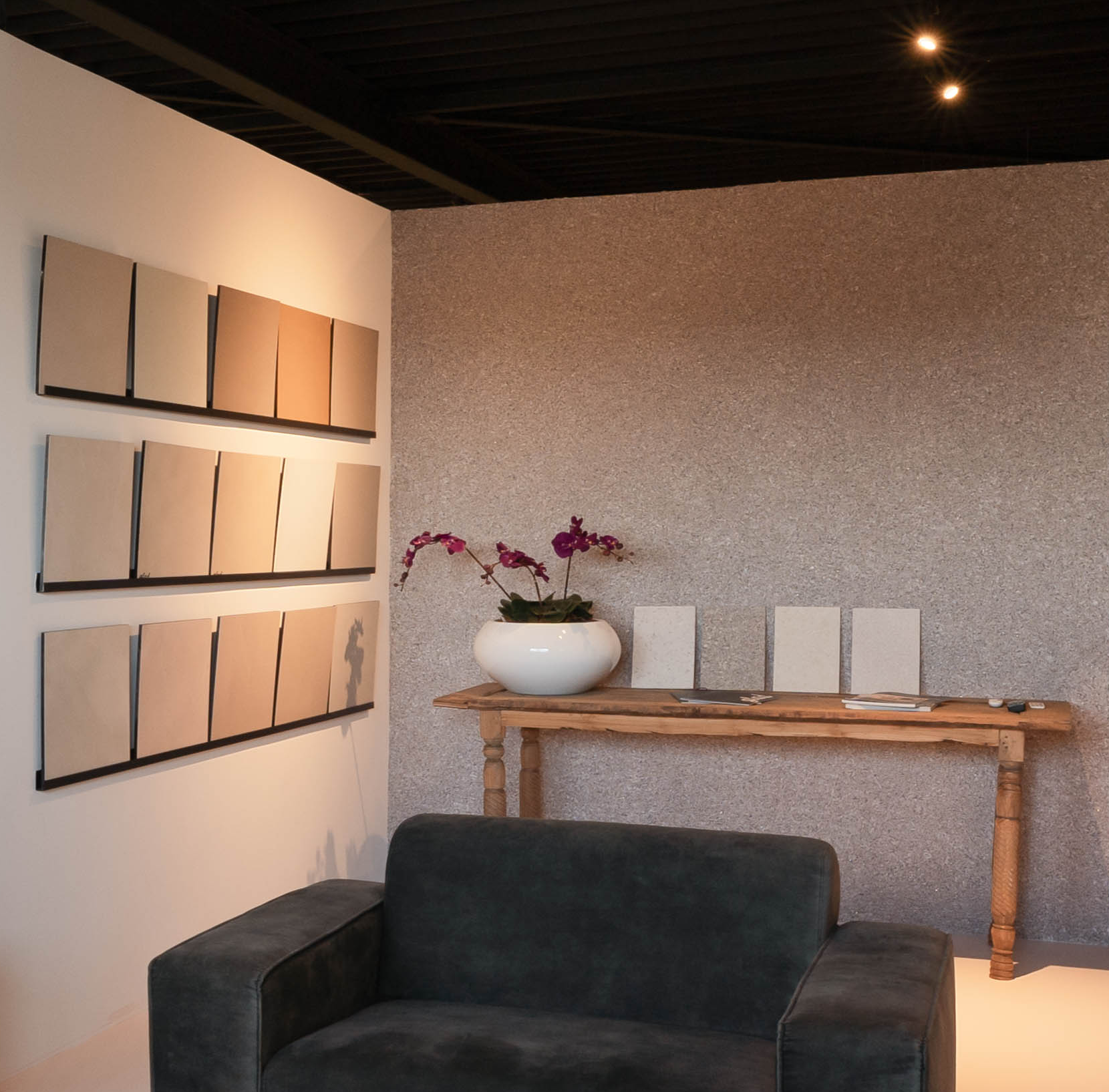 Gietvloer showroom met kleurstalen aan de muur, houten tafel met tegelsamples en een katoen wand afwerking